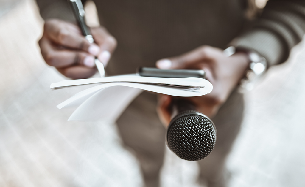 Writing notes on paper while holding microphone.